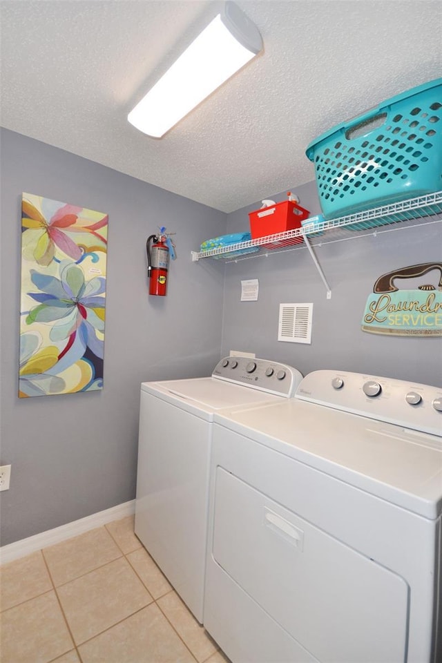 laundry room with washing machine and clothes dryer, light tile patterned floors, and a textured ceiling