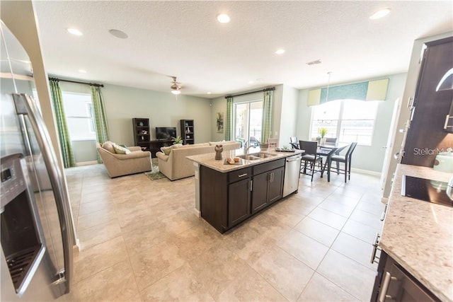 kitchen featuring light stone counters, stainless steel dishwasher, dark brown cabinets, sink, and pendant lighting