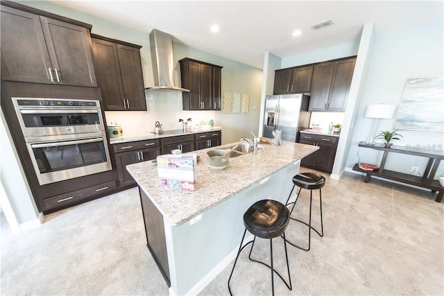 kitchen with sink, wall chimney exhaust hood, a kitchen breakfast bar, an island with sink, and appliances with stainless steel finishes