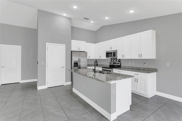 kitchen with appliances with stainless steel finishes, tile patterned floors, sink, stone counters, and an island with sink