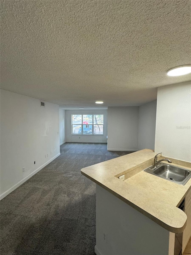 kitchen featuring dark colored carpet, kitchen peninsula, sink, and a textured ceiling