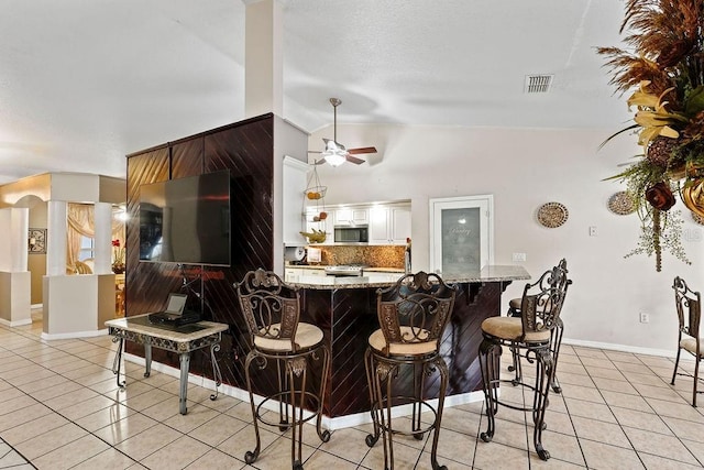 kitchen with kitchen peninsula, decorative backsplash, appliances with stainless steel finishes, light stone counters, and white cabinetry