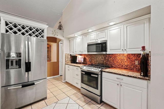 kitchen with arched walkways, light tile patterned floors, stone counters, white cabinets, and appliances with stainless steel finishes