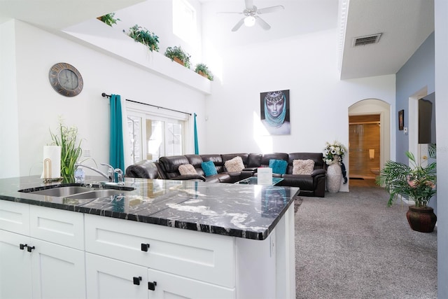 kitchen featuring a towering ceiling, light colored carpet, white cabinetry, and sink