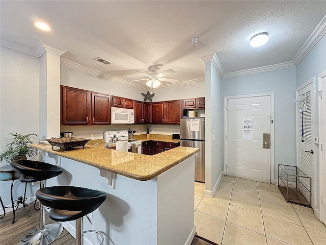 kitchen with a textured ceiling, appliances with stainless steel finishes, light tile patterned flooring, kitchen peninsula, and a breakfast bar area