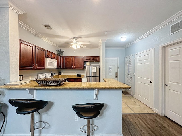 kitchen featuring stainless steel refrigerator, ceiling fan, kitchen peninsula, a kitchen bar, and ornamental molding