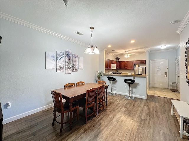 dining room featuring a textured ceiling, ceiling fan with notable chandelier, light hardwood / wood-style flooring, and crown molding