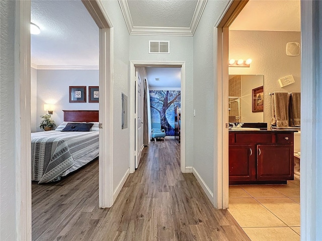 hallway featuring a textured ceiling, light wood-type flooring, crown molding, and sink