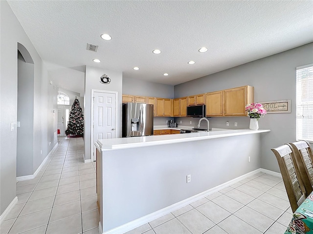 kitchen featuring stove, kitchen peninsula, light tile patterned floors, a textured ceiling, and stainless steel fridge with ice dispenser