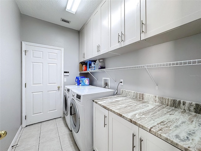 laundry room with washing machine and dryer, light tile patterned floors, cabinets, and a textured ceiling