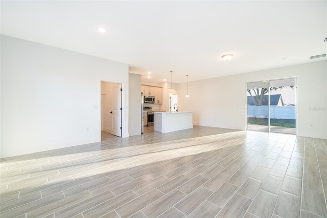 unfurnished living room featuring recessed lighting, visible vents, a sink, light wood-type flooring, and baseboards