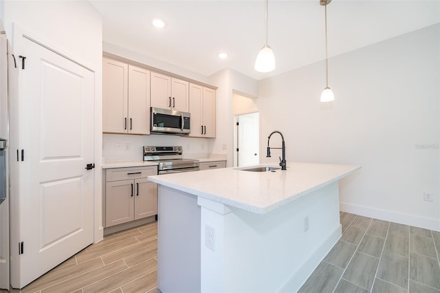 kitchen with decorative light fixtures, stainless steel appliances, wood tiled floor, a kitchen island with sink, and a sink