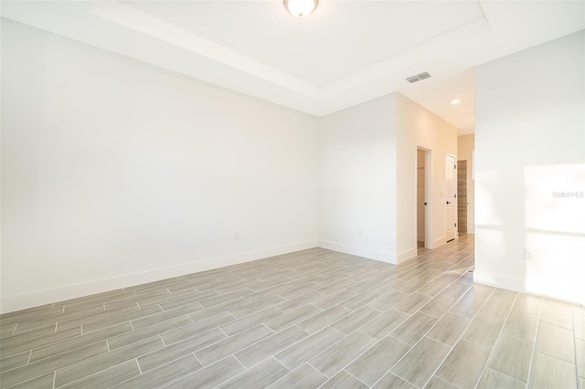 spare room with light wood-type flooring, baseboards, visible vents, and a tray ceiling