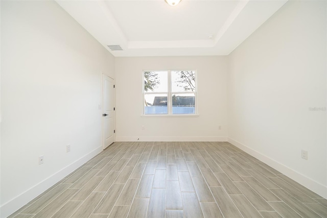 empty room featuring wood tiled floor, a raised ceiling, visible vents, and baseboards