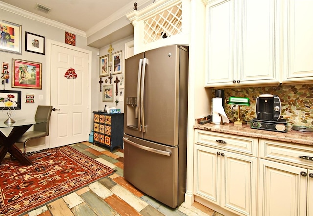 kitchen with light stone countertops, backsplash, crown molding, cream cabinets, and stainless steel fridge with ice dispenser