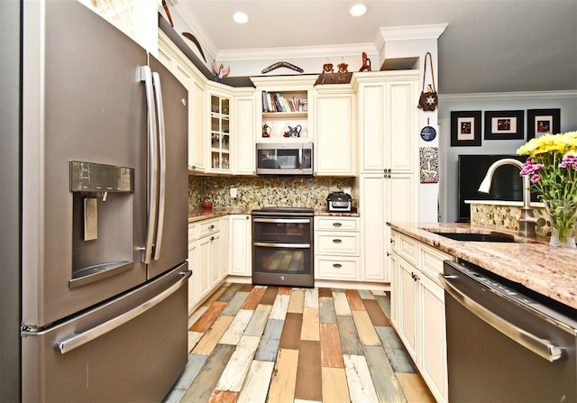 kitchen featuring sink, light stone counters, backsplash, cream cabinets, and appliances with stainless steel finishes