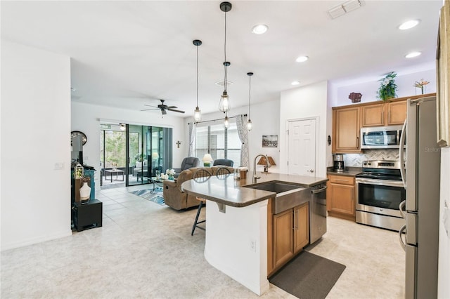 kitchen featuring a kitchen breakfast bar, stainless steel appliances, ceiling fan, a kitchen island with sink, and sink