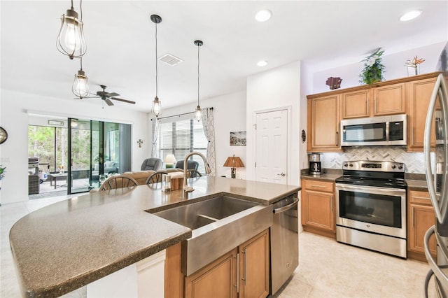 kitchen with stainless steel appliances, ceiling fan, a kitchen island with sink, sink, and hanging light fixtures