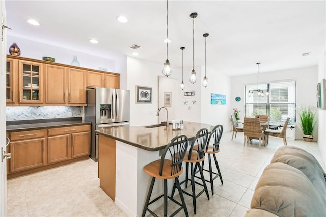 kitchen with decorative backsplash, stainless steel fridge, sink, a center island with sink, and hanging light fixtures