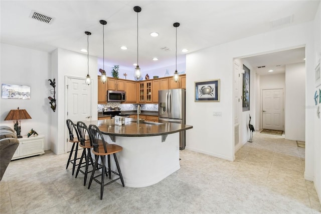 kitchen featuring decorative backsplash, appliances with stainless steel finishes, a kitchen island with sink, sink, and a breakfast bar area