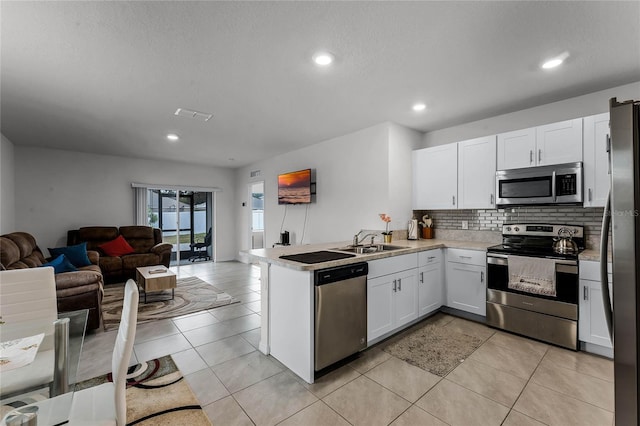 kitchen with kitchen peninsula, appliances with stainless steel finishes, sink, white cabinets, and light tile patterned flooring