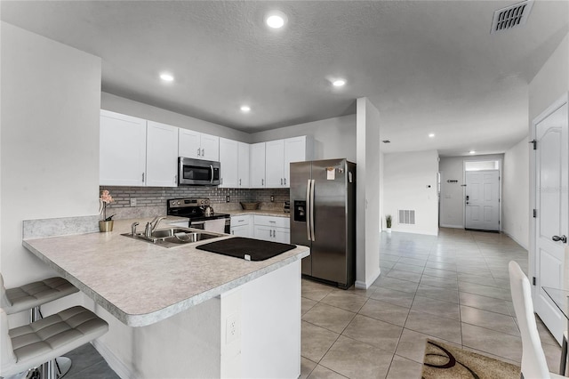 kitchen with white cabinets, sink, appliances with stainless steel finishes, a kitchen bar, and kitchen peninsula