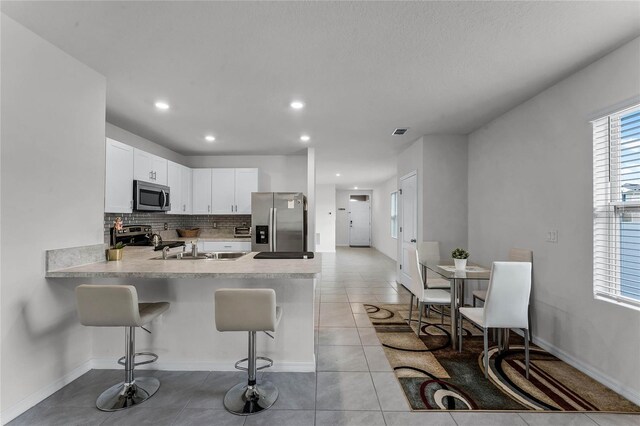 kitchen with a kitchen bar, tasteful backsplash, stainless steel appliances, white cabinetry, and light tile patterned flooring