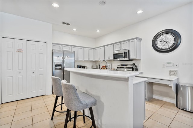 kitchen with a kitchen bar, light tile patterned floors, stainless steel appliances, and decorative backsplash