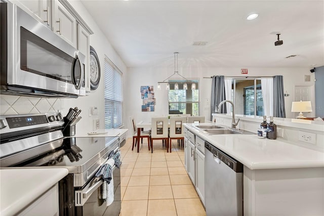 kitchen with sink, stainless steel appliances, backsplash, pendant lighting, and light tile patterned floors