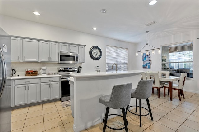 kitchen with pendant lighting, stainless steel appliances, light tile patterned floors, and a kitchen island with sink