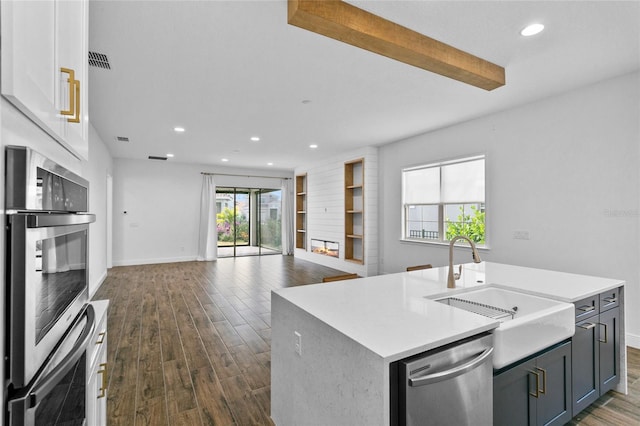 kitchen with sink, dark hardwood / wood-style floors, an island with sink, appliances with stainless steel finishes, and beamed ceiling