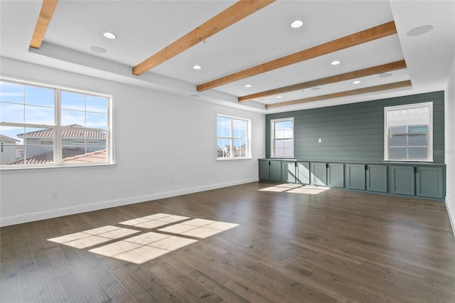 empty room featuring beam ceiling, dark hardwood / wood-style flooring, and a wealth of natural light