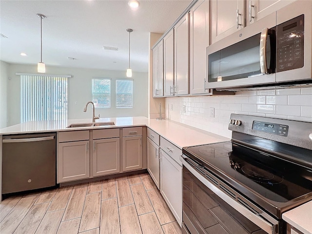 kitchen with sink, gray cabinetry, hanging light fixtures, kitchen peninsula, and stainless steel appliances