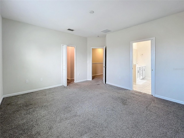 unfurnished bedroom featuring a walk in closet, ensuite bath, and carpet