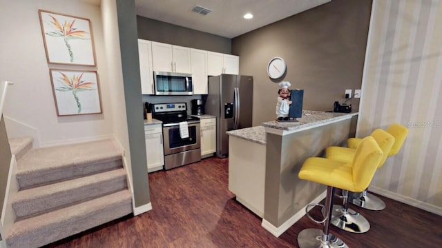 kitchen featuring stainless steel appliances, light stone counters, kitchen peninsula, a kitchen bar, and white cabinets