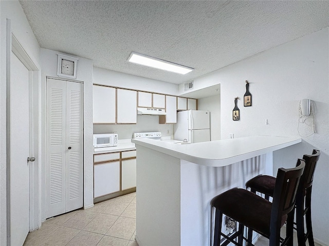 kitchen featuring kitchen peninsula, a kitchen bar, white appliances, and white cabinets