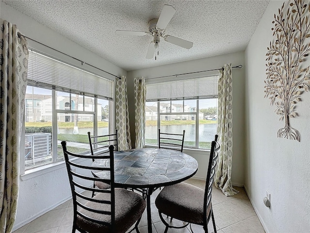 dining space with ceiling fan, a water view, light tile patterned flooring, and a textured ceiling