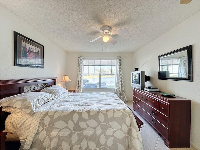 bedroom featuring ceiling fan, light tile patterned floors, and a textured ceiling