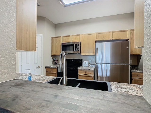 kitchen with light brown cabinets, stainless steel appliances, and light stone counters