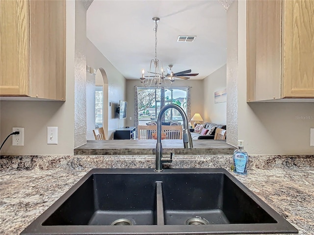 kitchen with light brown cabinets, light stone counters, sink, and a chandelier