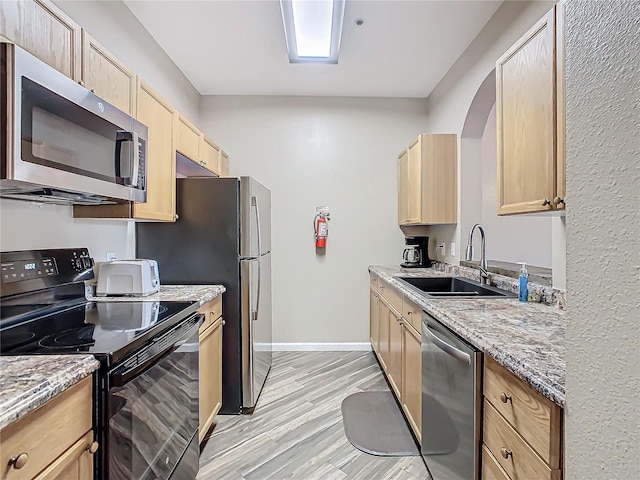 kitchen featuring light stone countertops, stainless steel appliances, sink, light brown cabinets, and light hardwood / wood-style flooring