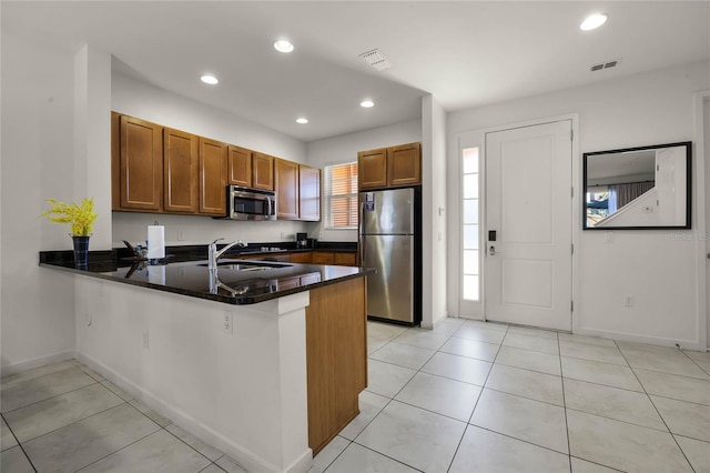 kitchen featuring sink, kitchen peninsula, dark stone countertops, light tile patterned flooring, and appliances with stainless steel finishes