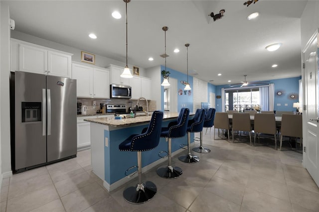 kitchen with white cabinets, light stone counters, an island with sink, and stainless steel appliances