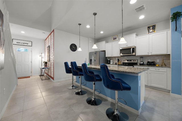 kitchen with stone counters, stainless steel appliances, an island with sink, decorative light fixtures, and white cabinets