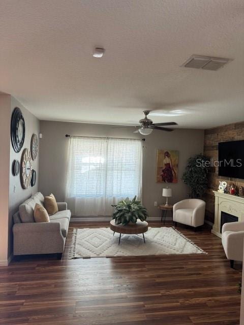 living room with ceiling fan, a large fireplace, dark hardwood / wood-style flooring, and a textured ceiling