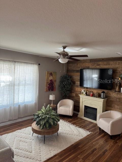 living room with dark hardwood / wood-style flooring, ceiling fan, and a textured ceiling