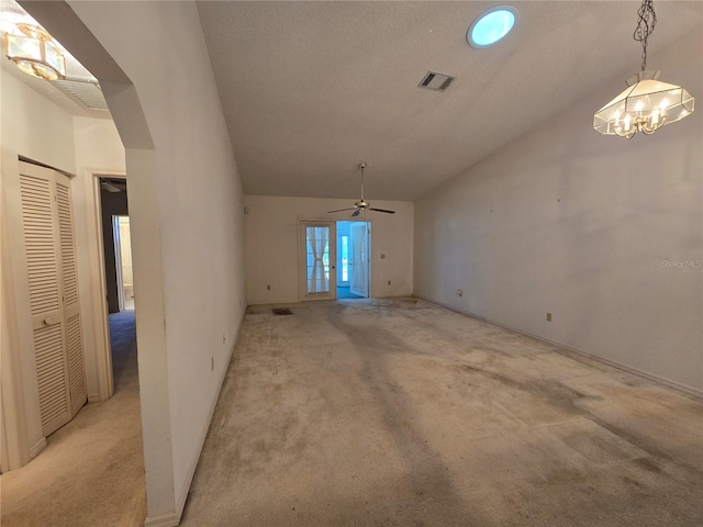 unfurnished living room featuring ceiling fan with notable chandelier, light colored carpet, and vaulted ceiling