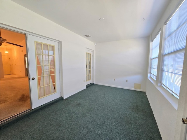 spare room featuring a wealth of natural light, ceiling fan, and dark colored carpet