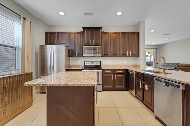 kitchen featuring light stone countertops, light tile patterned floors, appliances with stainless steel finishes, dark brown cabinets, and sink