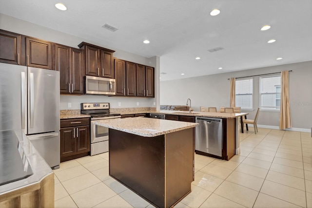 kitchen with stainless steel appliances, sink, light tile patterned floors, kitchen peninsula, and a kitchen island